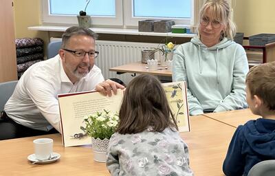 Landrat Alexander Tönnies zeigt Kindern, die vor ihm sitzen, die Bilder in einem Buch.