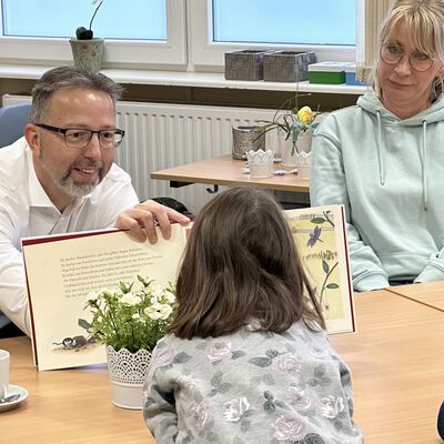 Landrat Alexander Tönnies zeigt Kindern, die vor ihm sitzen, die Bilder in einem Buch.